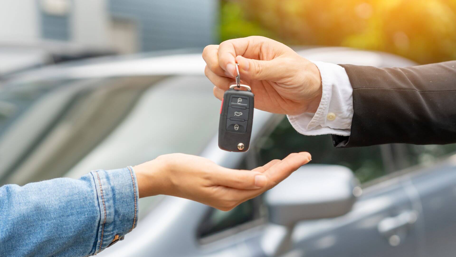 A person hands over car keys to another individual, with a car in the background, perhaps as part of a seamless roadside assistance service.